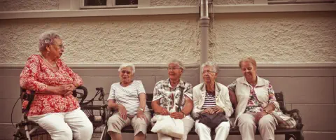 4 Frauen, die auf einer Bank sitzen, und eine Frau, die auf ihren Rollator sitzt.