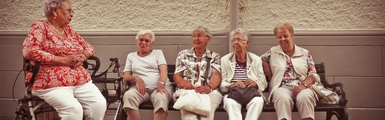 4 Frauen, die auf einer Bank sitzen, und eine Frau, die auf ihren Rollator sitzt.